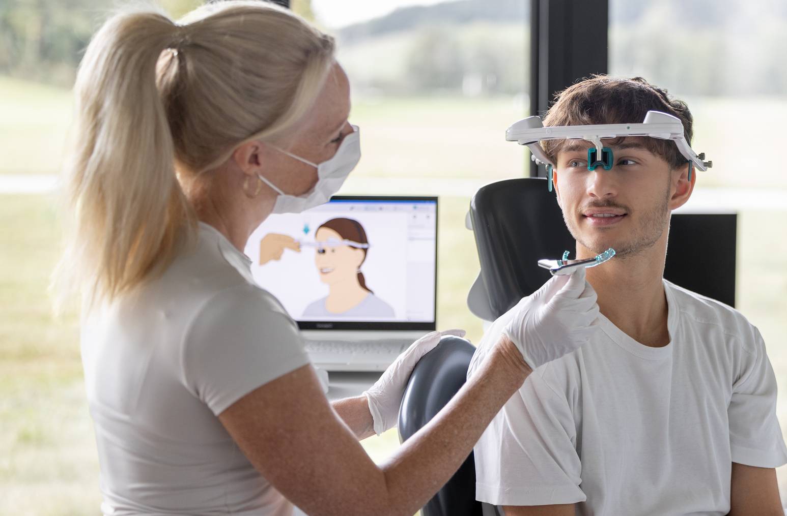 Zahnärztin justiert ein Gesichtsbogen-Messgerät bei einem jungen Patienten in moderner Praxisumgebung.